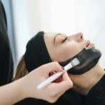 Close-up of a woman enjoying a relaxing charcoal facial treatment in a spa.